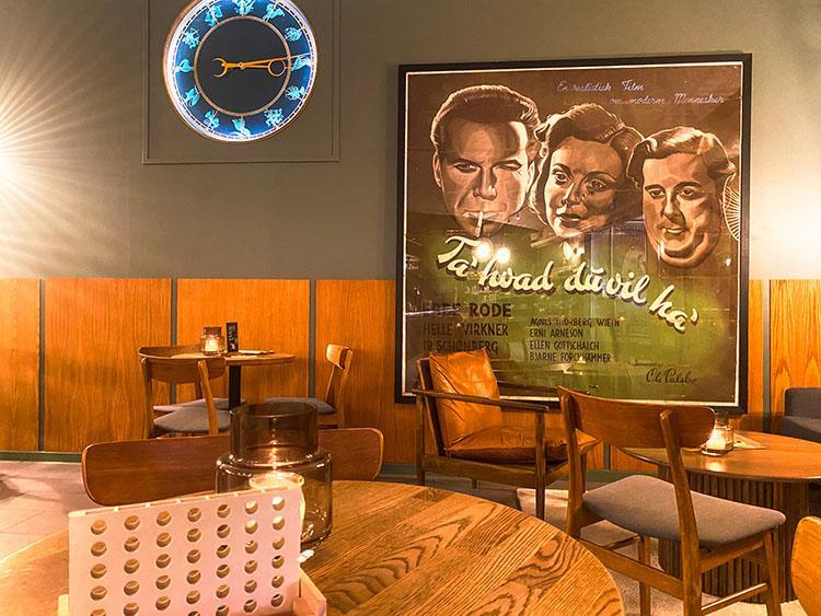 Caféområde med vintage filmplakat og ur hos Nordisk Film Biografer Trøjborg