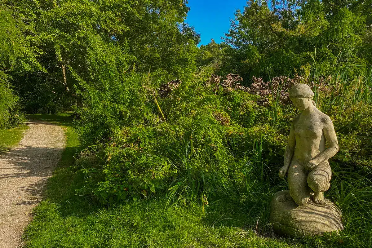 Stenstatue ved grøn beplantning langs stien i Forstbotanisk Have
