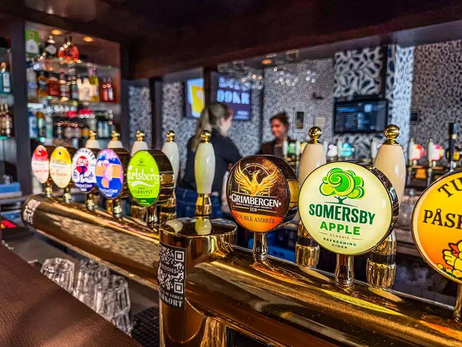 Freddies English Pub i Aarhus med over 16 forskellige ølhaner, mørkt træ, neonskilte og sportsskærme i baggrunden.