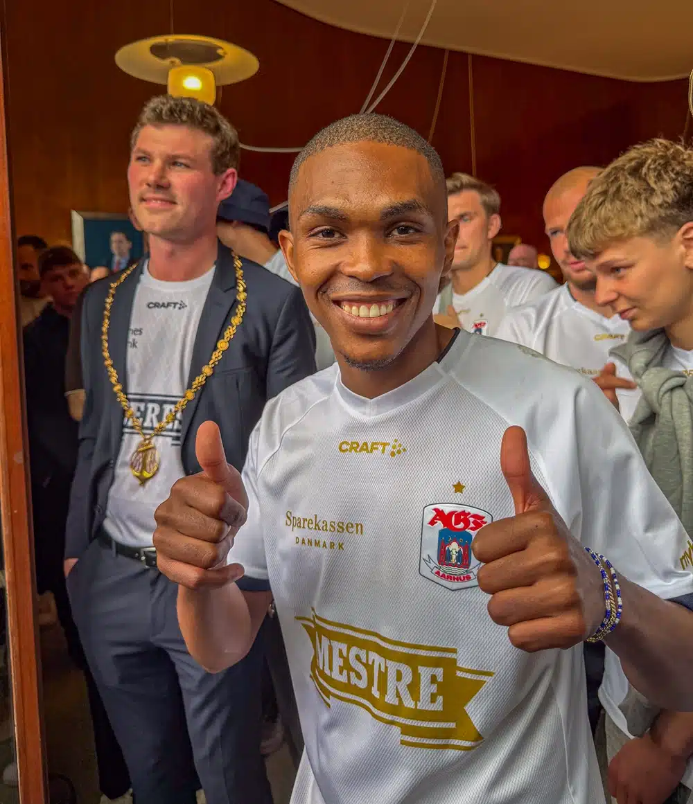En glad AGF-spiller i Mestre-trøjen viser tomlerne op, mens borgmester Anders Winnerskjold med den røde rådhuskæde om halsen står smilende bagved