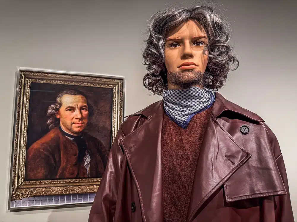Mandlig mannequin med grå krøllet parryk spejler 1700-tals portræt på The Populace på ARoS