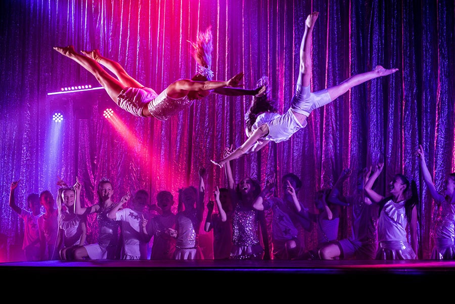 To unge gymnaster svaever gennem luften over scenen til Flying Superkids show » Aarhus Inside Flying Superkids i Aarhus: når 40 unge mennesker tager dig med ind i et fællesskab