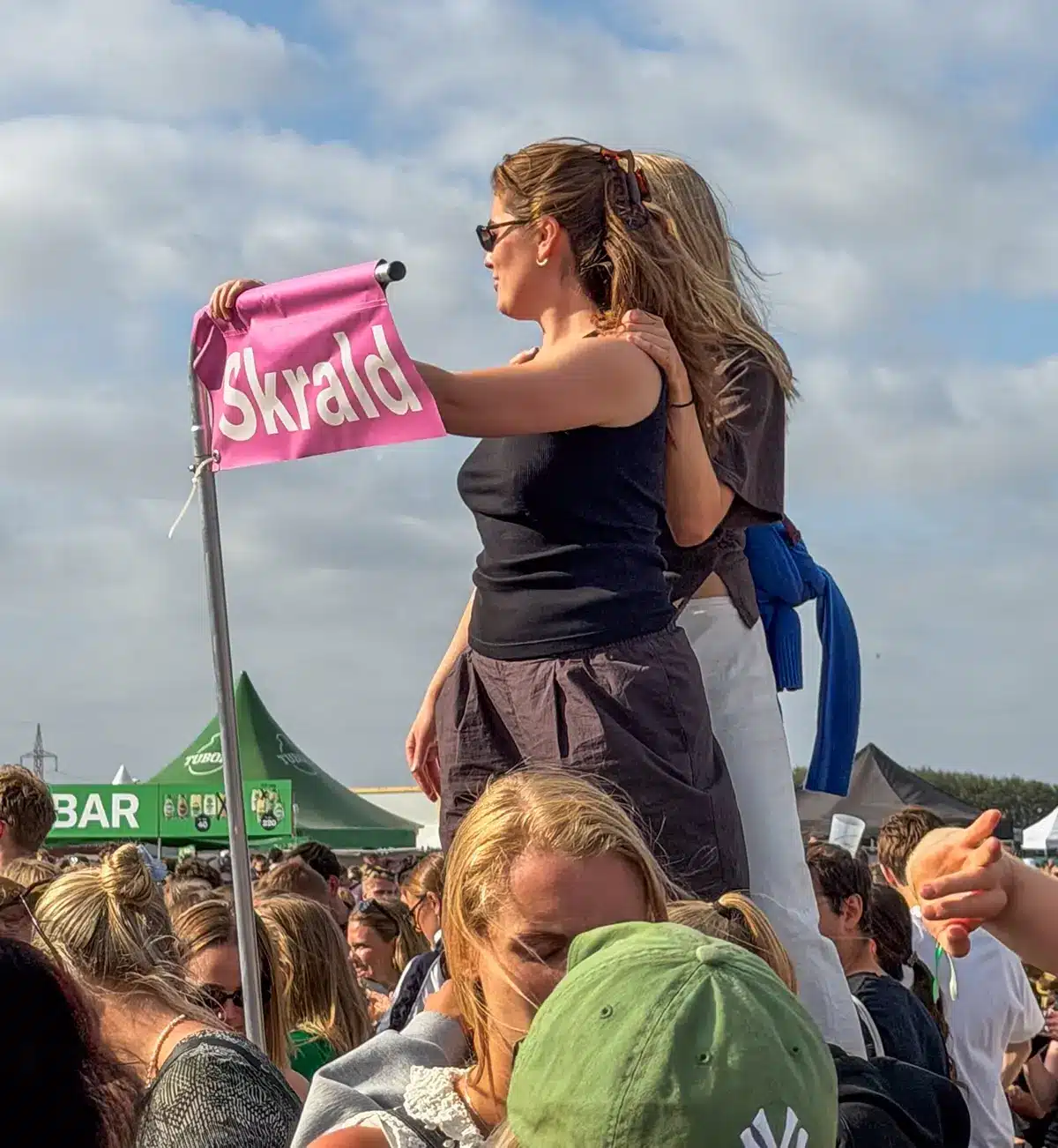 Festivalgæster foran et skilt med teksten skrald Festivalgæster foran et skilt med teksten skrald