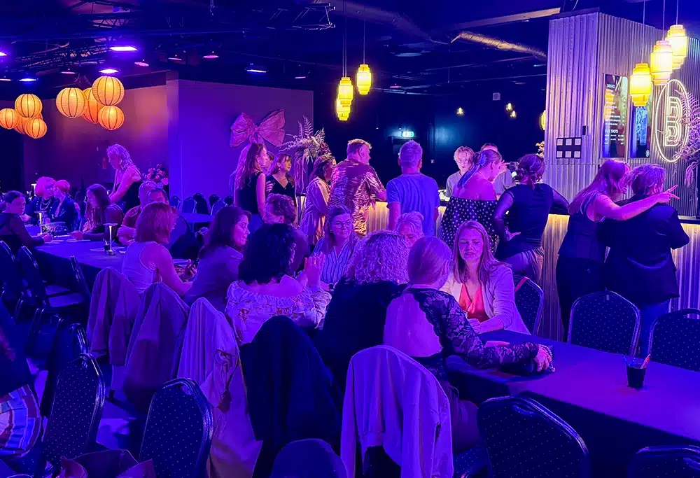 Fyldt lokale med gæster ved langborde i The Ballroom Fyldt lokale med gæster ved langborde i The Ballroom